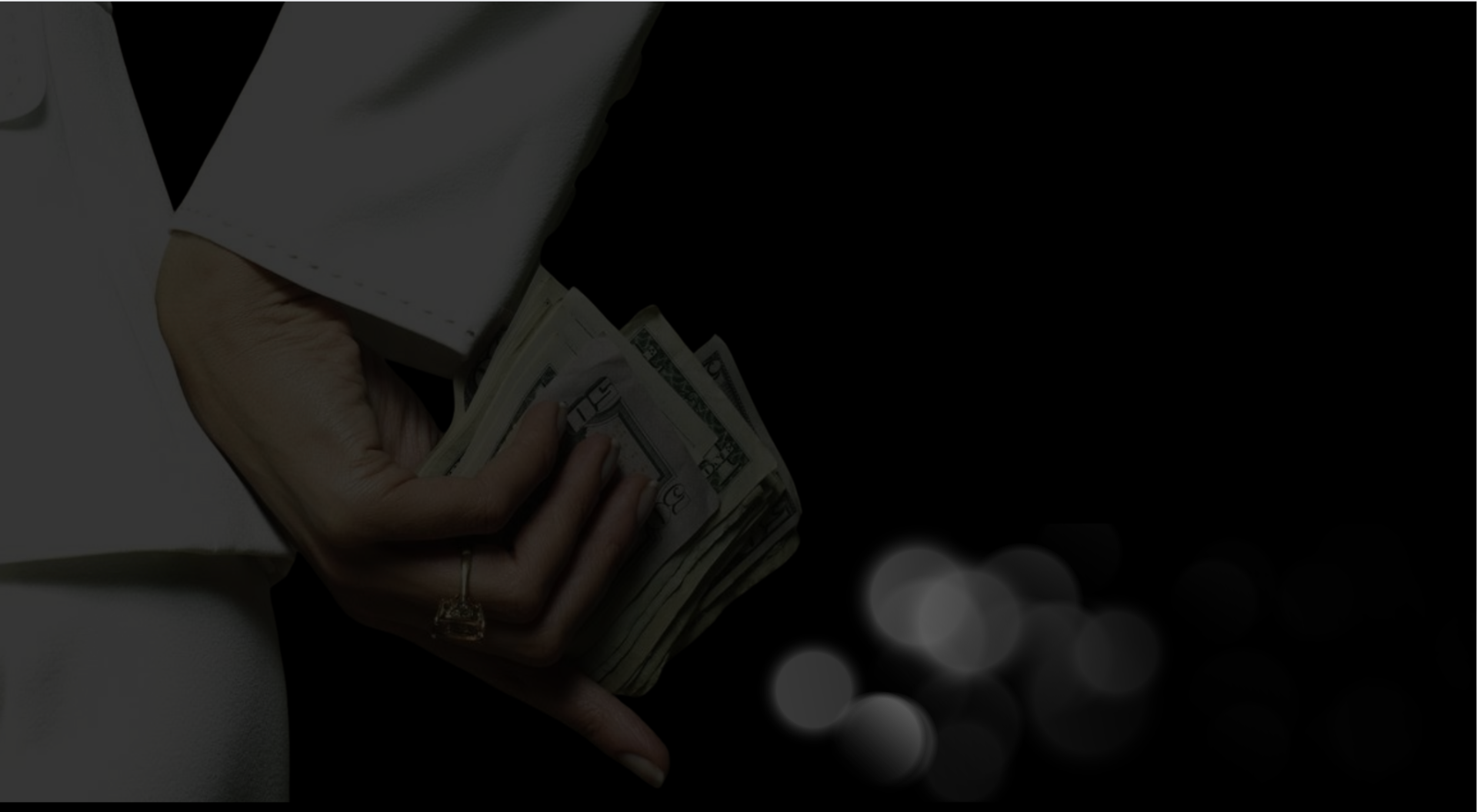 A hand holding a fan of cash against a dark background